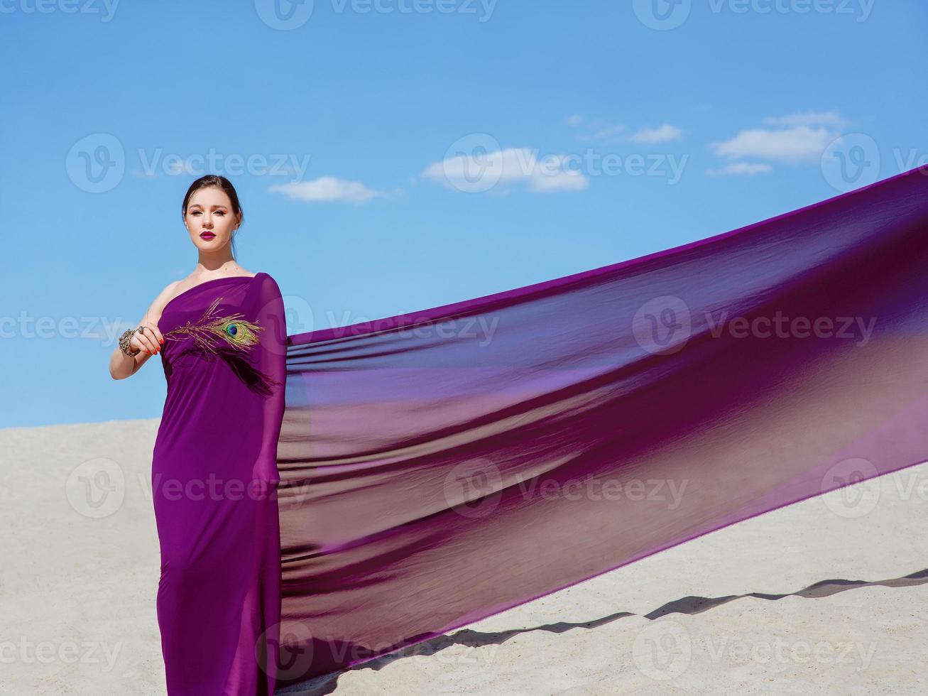 erstaunlich schöne brünette frau mit der pfauenfeder in lila stoff in der wüste. orientalisch, indisch, mode, stilkonzept foto