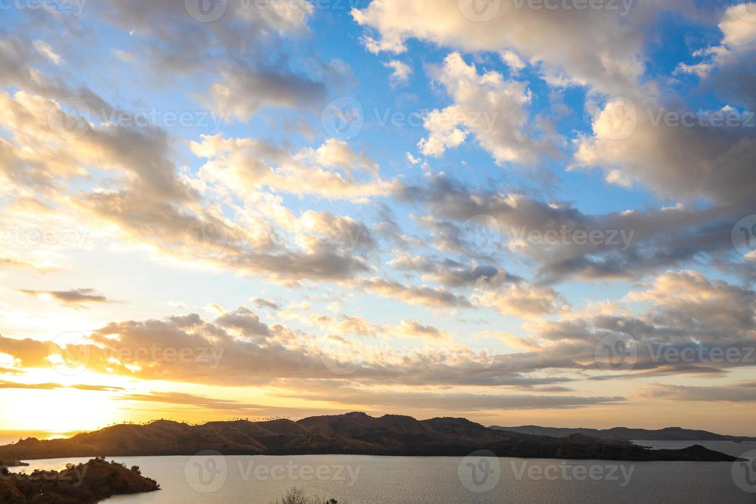 schöner sonnenuntergang auf dem meer mit hügeln und sonne, die unter wolkenhimmel herunterkommt foto