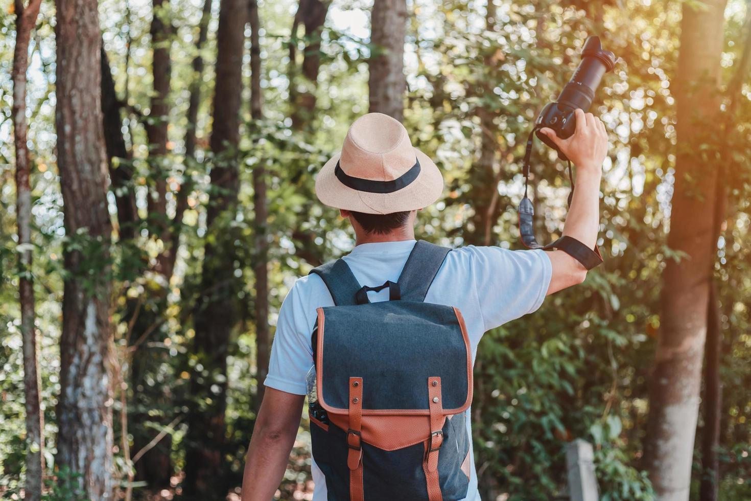 Ein männlicher Tourist mit Handtasche, Wasserflasche und Kamera geht durch den Wald. foto