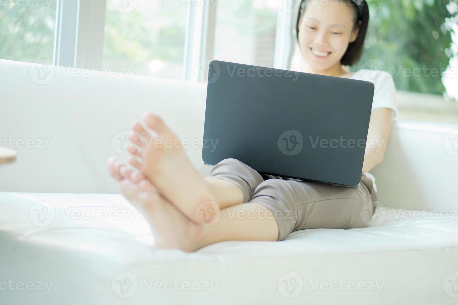 Lächelnde, glückliche Frau, die auf dem Sofa sitzt und Laptop benutzt - erhöhte Ansicht foto