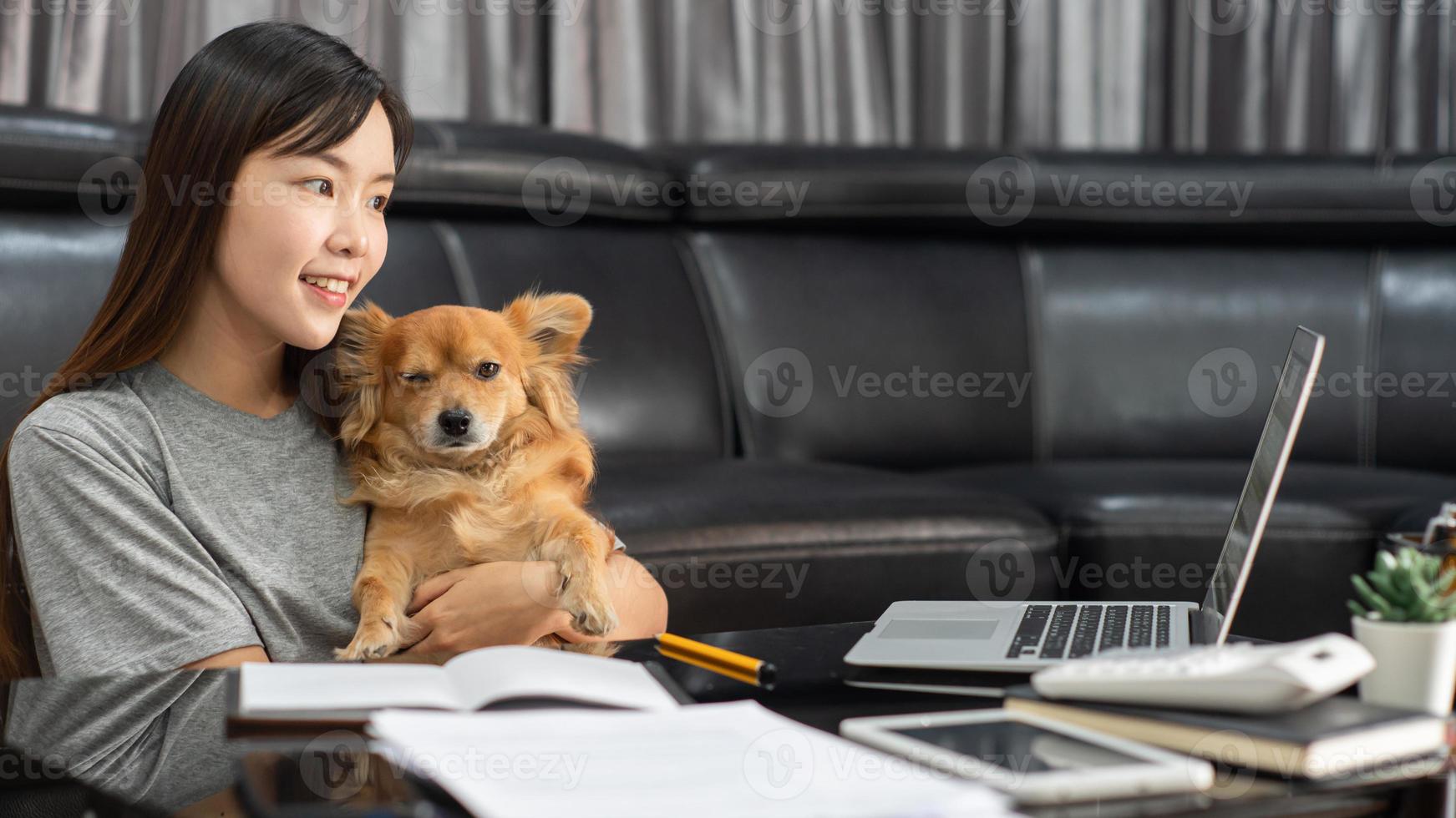 schöne junge asiatische frau, die fern von zu hause aus arbeitet und beim liegen lächelt, hat gute beziehungen zu einem lustigen assistenzhund, haustierkonzept für hausarbeit. foto