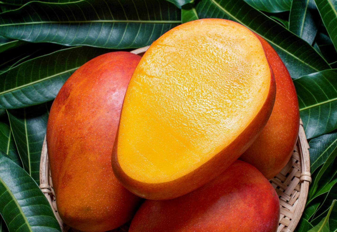 frische saftige schöne Mangofrucht im Bambusholzkorb auf grünem Hintergrund durch Blätter, Abschluss oben, Makro, Kopienraum. tropisches sommererntekonzept foto