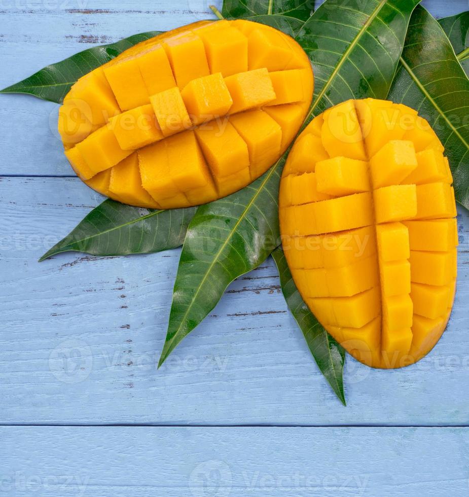 frische mango - schöne gehackte frucht mit grünen blättern auf hellblauem holzhintergrund. Designkonzept für tropische Früchte. flach liegen. Ansicht von oben. Platz kopieren foto