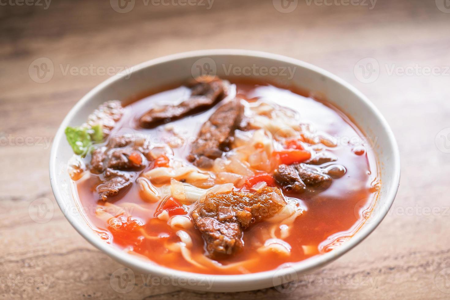 Rindfleisch-Nudel-Ramen-Mahlzeit mit Tomatensauce-Brühe in Schüssel auf hellem Holztisch, berühmtes Essen im chinesischen Stil in Taiwan, Nahaufnahme, Draufsicht, Kopierraum foto