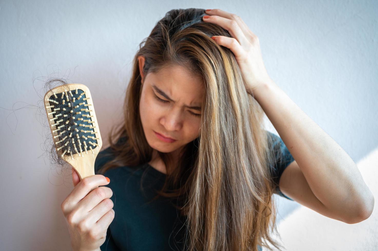 Besorgte Frau, die Kamm mit Haarausfall hält, nachdem sie sich die Haare gebürstet hat. Haarausfall, der durch Familiengeschichte, hormonelle Veränderungen, ungesundes Altern verursacht wird. foto