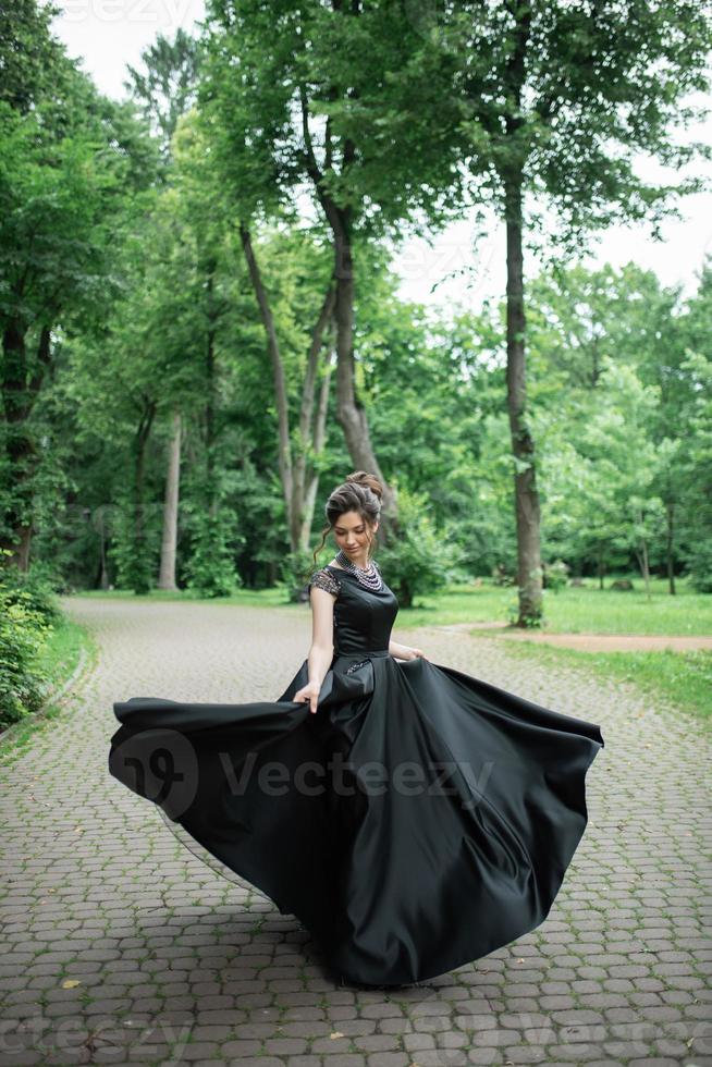 junge schöne frau, die in einem schwarzen kleid in einem park aufwirft. foto