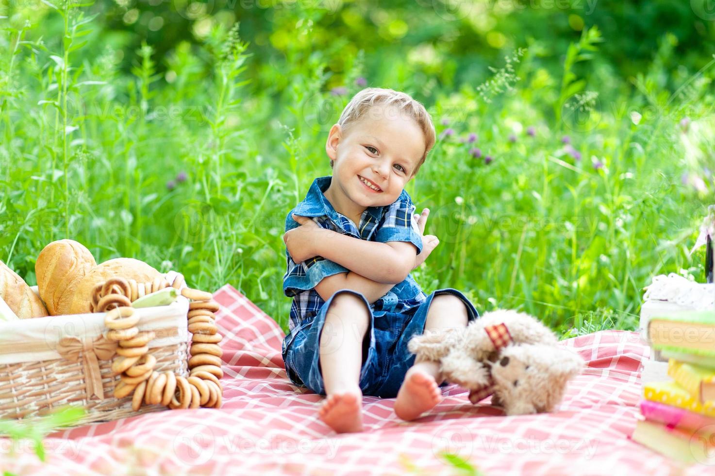 Ein kleiner süßer Junge sitzt auf einem Plaid und spielt mit seinem Teddybär. foto