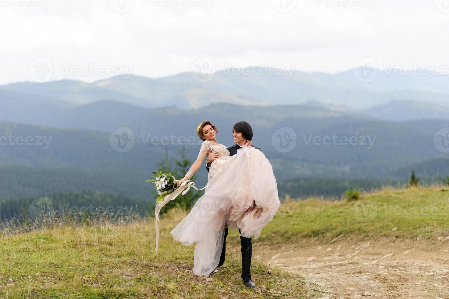 der bräutigam trägt seine braut in den armen. Hochzeitsfotografie in den Bergen. foto