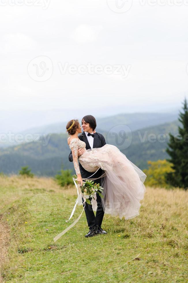 der bräutigam trägt seine braut in den armen. Hochzeitsfotografie in den Bergen. foto