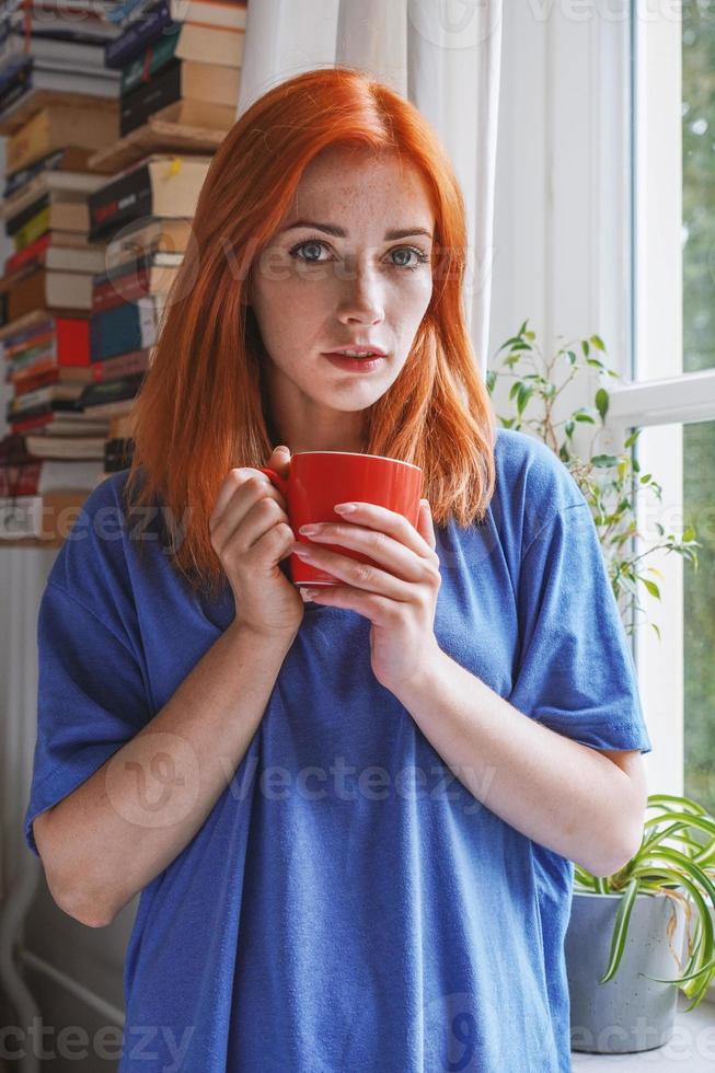 junge frau, die zu hause in ihrem wohnzimmer steht und eine kaffeetasse hält foto