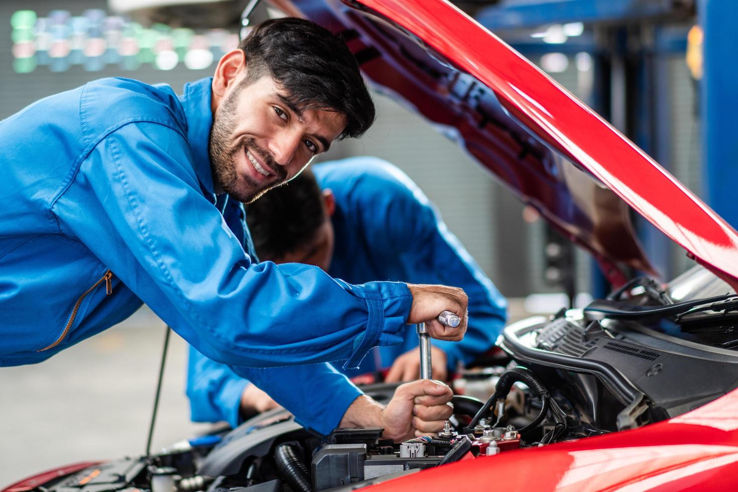 Fröhlicher lächelnder kaukasischer Kfz-Mechaniker, der den Zustand des beschädigten Teils des Fahrzeugs überprüft, das Fahrzeug in der Kfz-Werkstatt diagnostiziert und repariert, die Wartung des Motortechnikers nach dem Servicekonzept foto