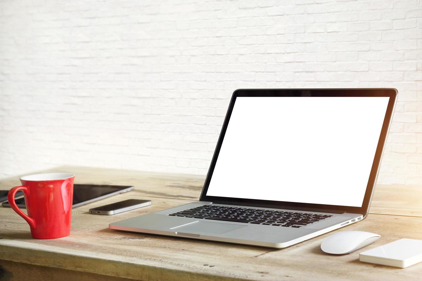 Laptop mit leerem weißen Bildschirm auf dem Tisch im weißen Backsteinmauerhintergrund foto