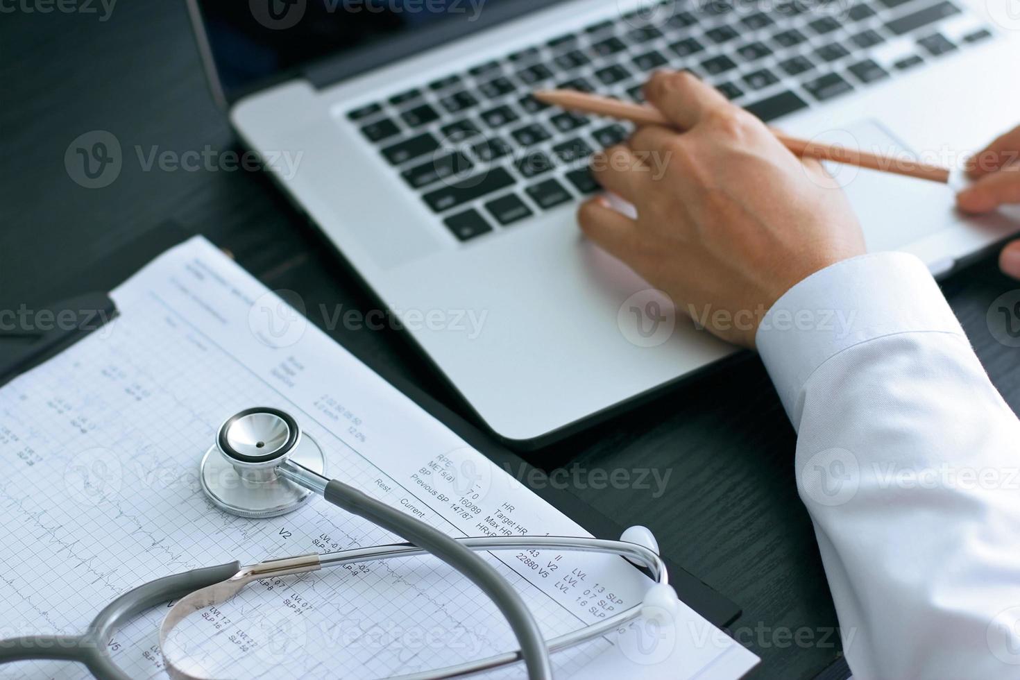 arzt, der einen laptop verwendet, der auf dem schreibtisch mit stethoskop arbeitet, um den bericht der patienten im gesundheitswesen zu überprüfen. Netzwerkkonzept Medizintechnik foto