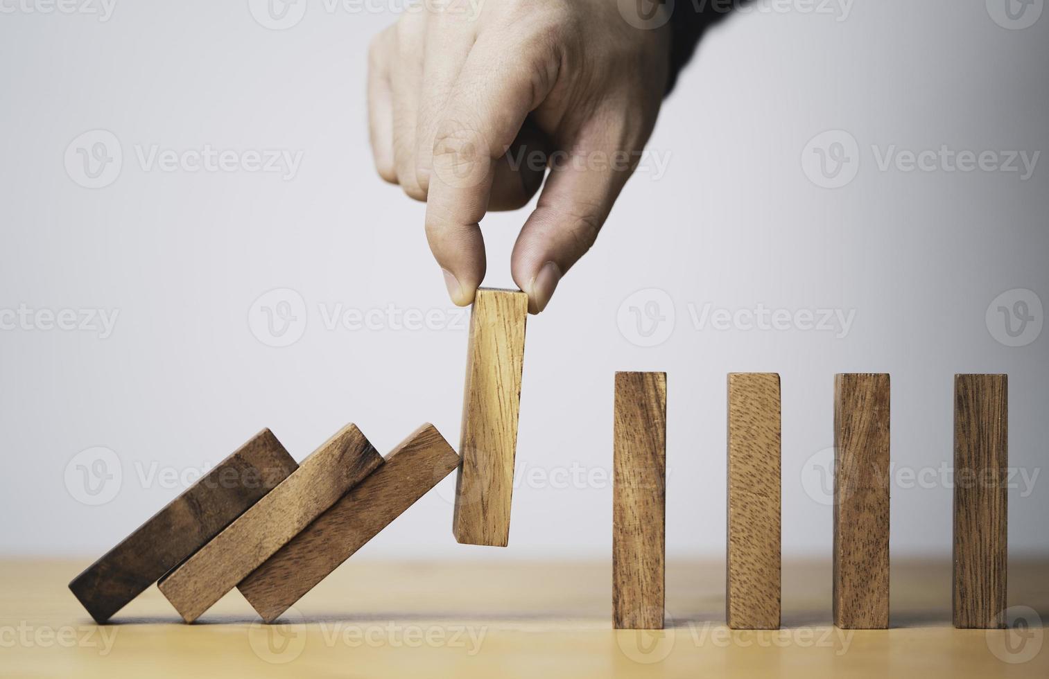 Ziehen Sie den Holzblock von Hand heraus, um das Herunterfallen von Dominosteinen zu verhindern und zu stoppen. Dies ist ein Symbol für den Schutz vor Schäden oder den Verluststopp für das Krisenmanagementkonzept foto