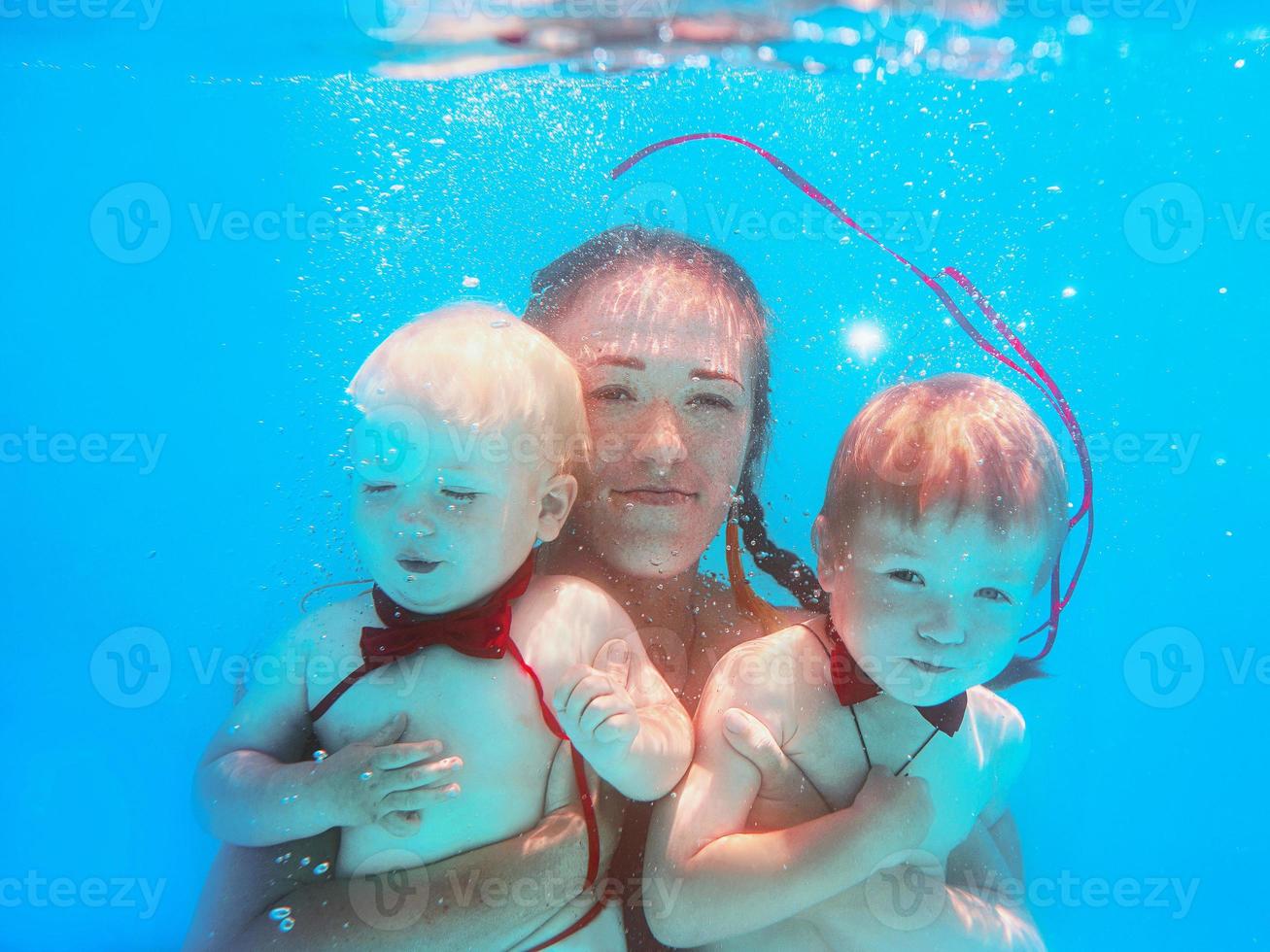 kaukasische frau mit kleinen jungen in roten schmetterlingen, die unter wasser im schwimmbad tauchen, schwimmen lernen. sport-, familien-, liebes- und urlaubskonzept foto