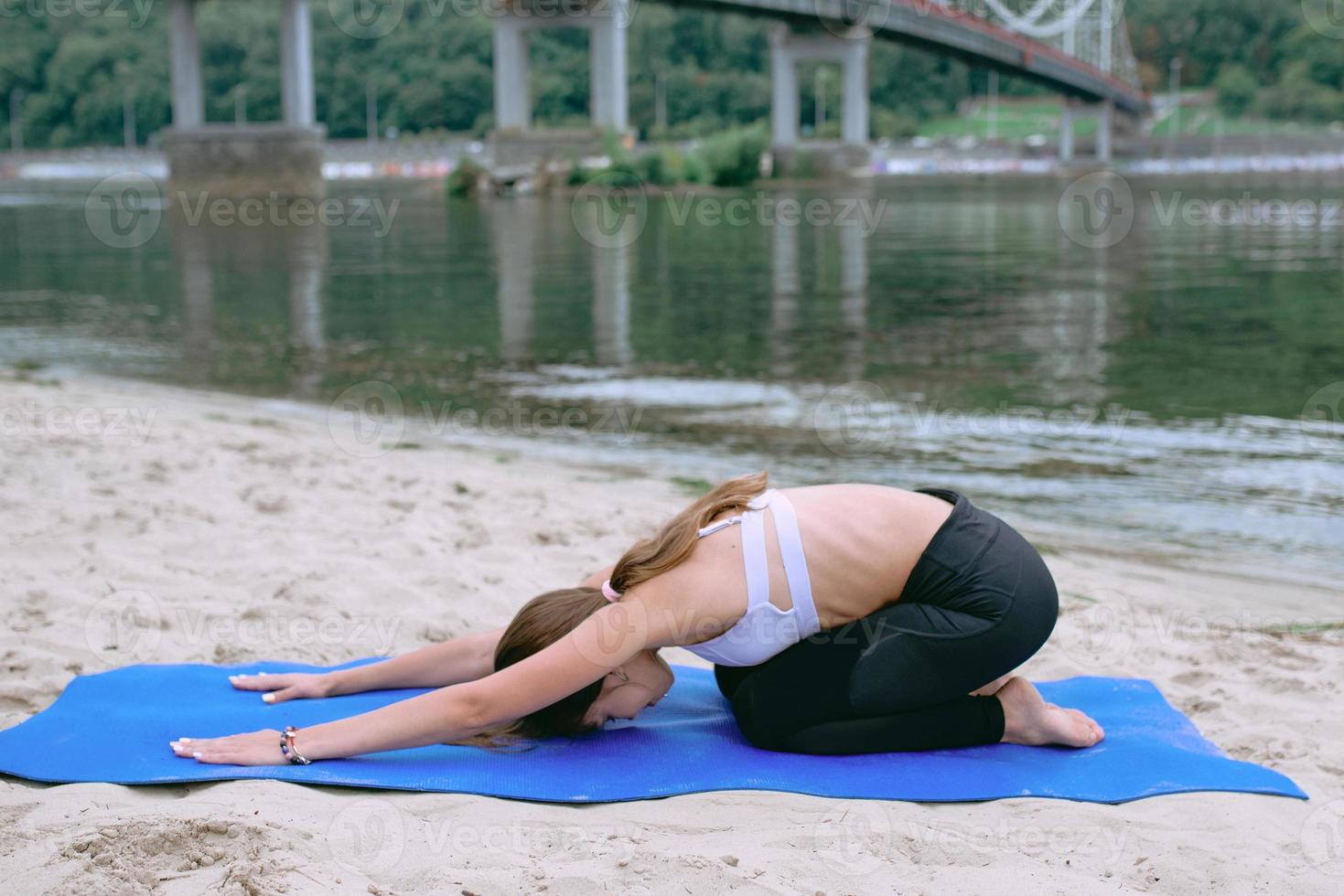 Junge fitte Frau in Sportbekleidung in verschiedenen Yoga-Asanas im Freien am Strand am Fluss. yoga- und sportkonzept foto