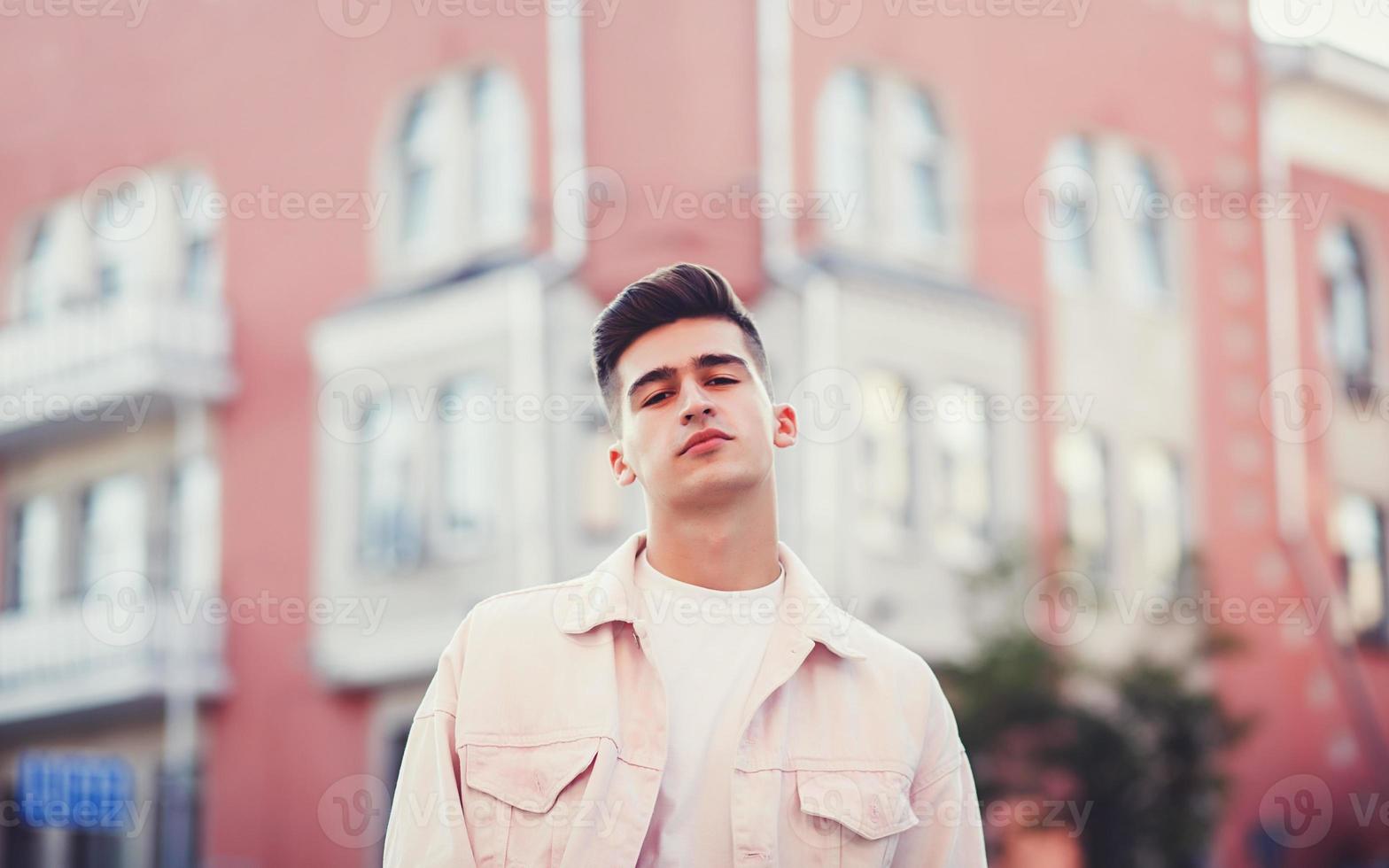 Stylischer Typ, der in einer Jeansjacke auf der Straße steht foto