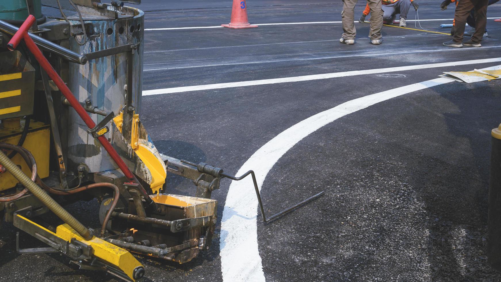 Nahaufnahme einer thermoplastischen Sprühmarkierungsmaschine mit verschwommenem Hintergrund des Straßenarbeiterteams, das Linien zum Streichen von Fußgängerüberwegen und Verkehrslinien auf Asphaltstraßen herstellt foto