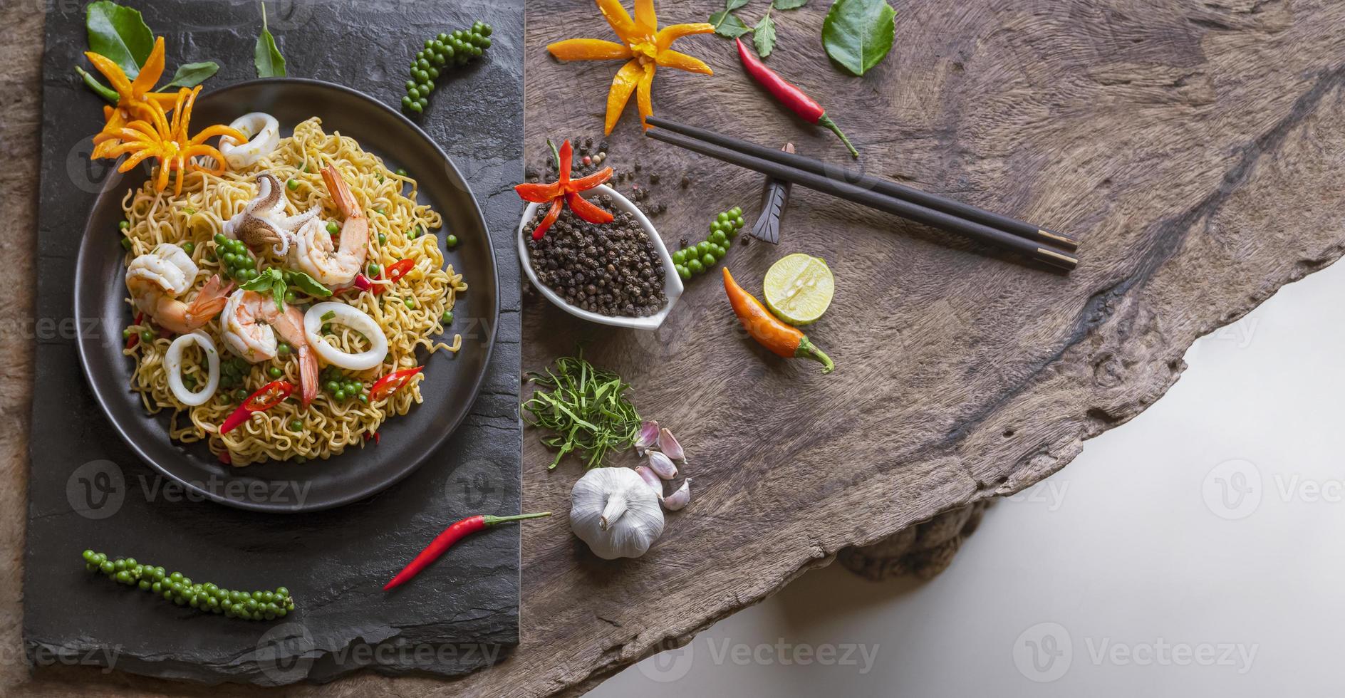 Draufsicht auf Instant-Nudeln mit gebratenen würzigen Meeresfrüchten und verschiedenen Gewürzen auf einer Holztischplatte im Vintage-Ton-Stil, Junk-Food und asiatischem Speisekonzept foto