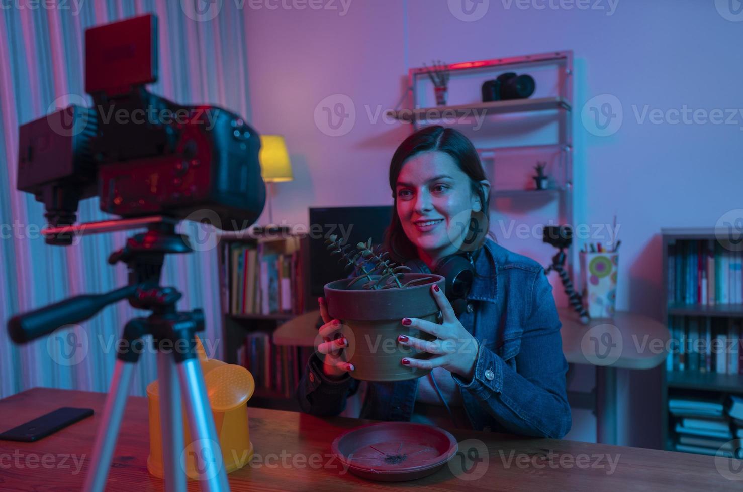Schöne hispanische Frau vor einer Videokamera, die einen Blog in ihrem Studio mit roten und blauen Lichtern in ihrem Haus aufzeichnet foto