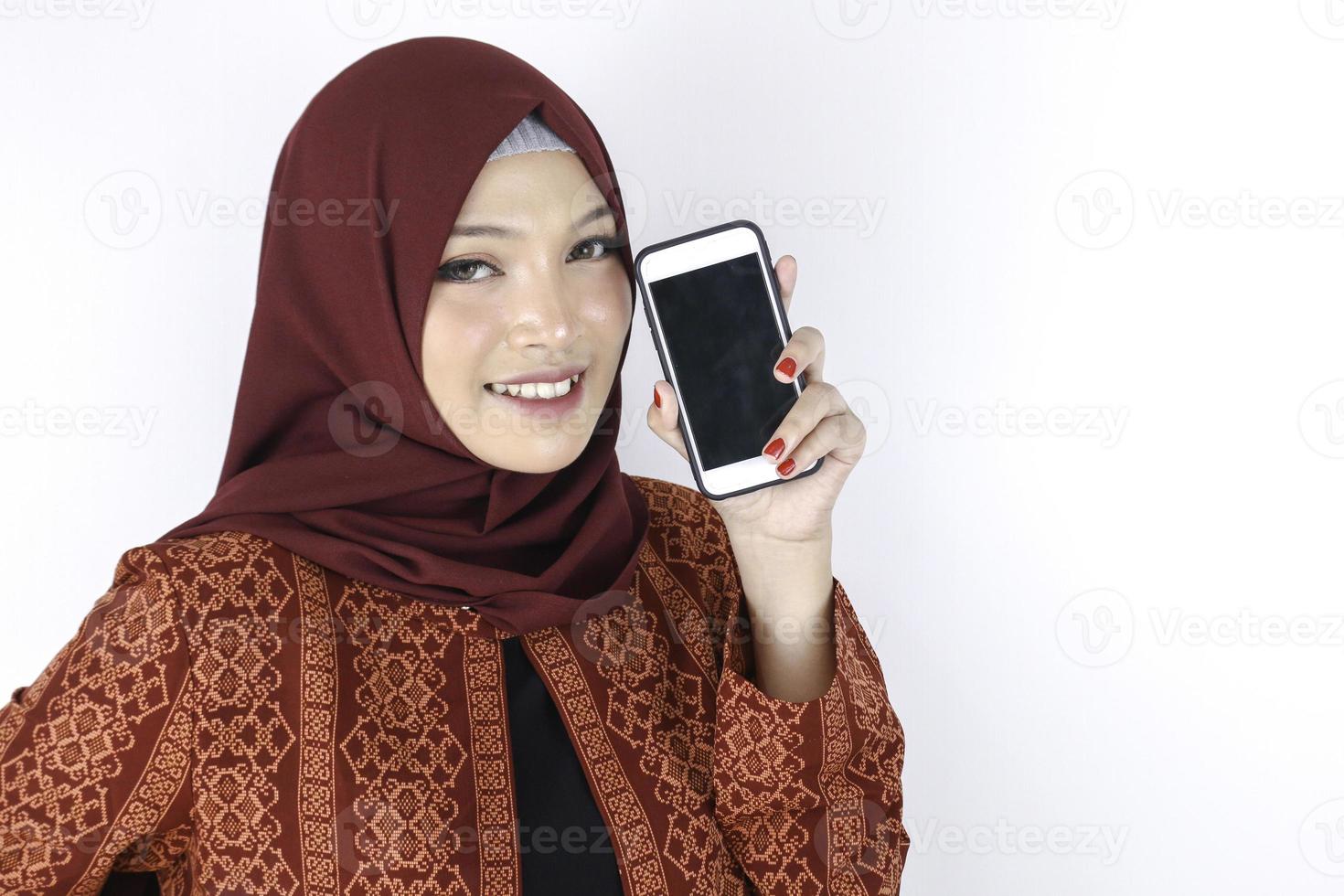 Junge asiatische Islamfrau lächelt und zeigt Smartphone auf weißem Hintergrund. foto