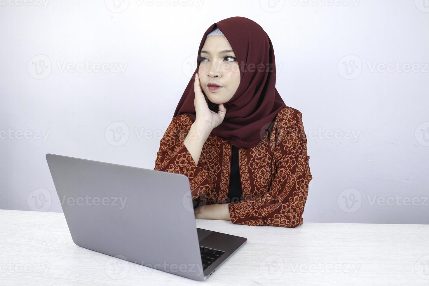 junge asiatische islamfrau ist ernster blick mit denkender geste hand auf gesicht auf der vorderseite des laptops. foto