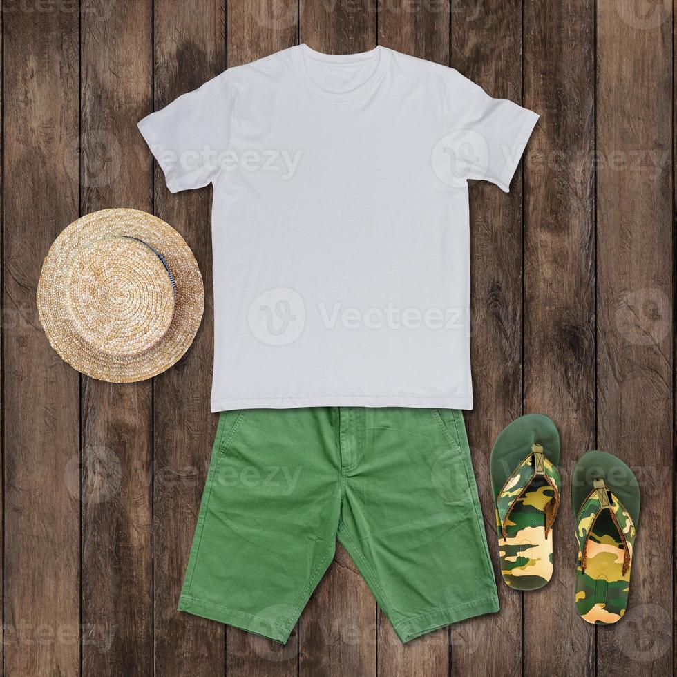 Weißes T-Shirt mit grünen Shorts, Sandalen, Hut auf dem Holzboden. foto