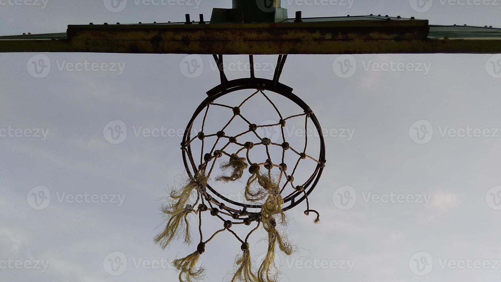 Ansicht von unten des dunkelgrünen alten Basketballkorbs und des zerbrochenen Netzes mit einem dunklen Hintergrund des Morgenhimmels auf dem öffentlichen Sportplatz. foto