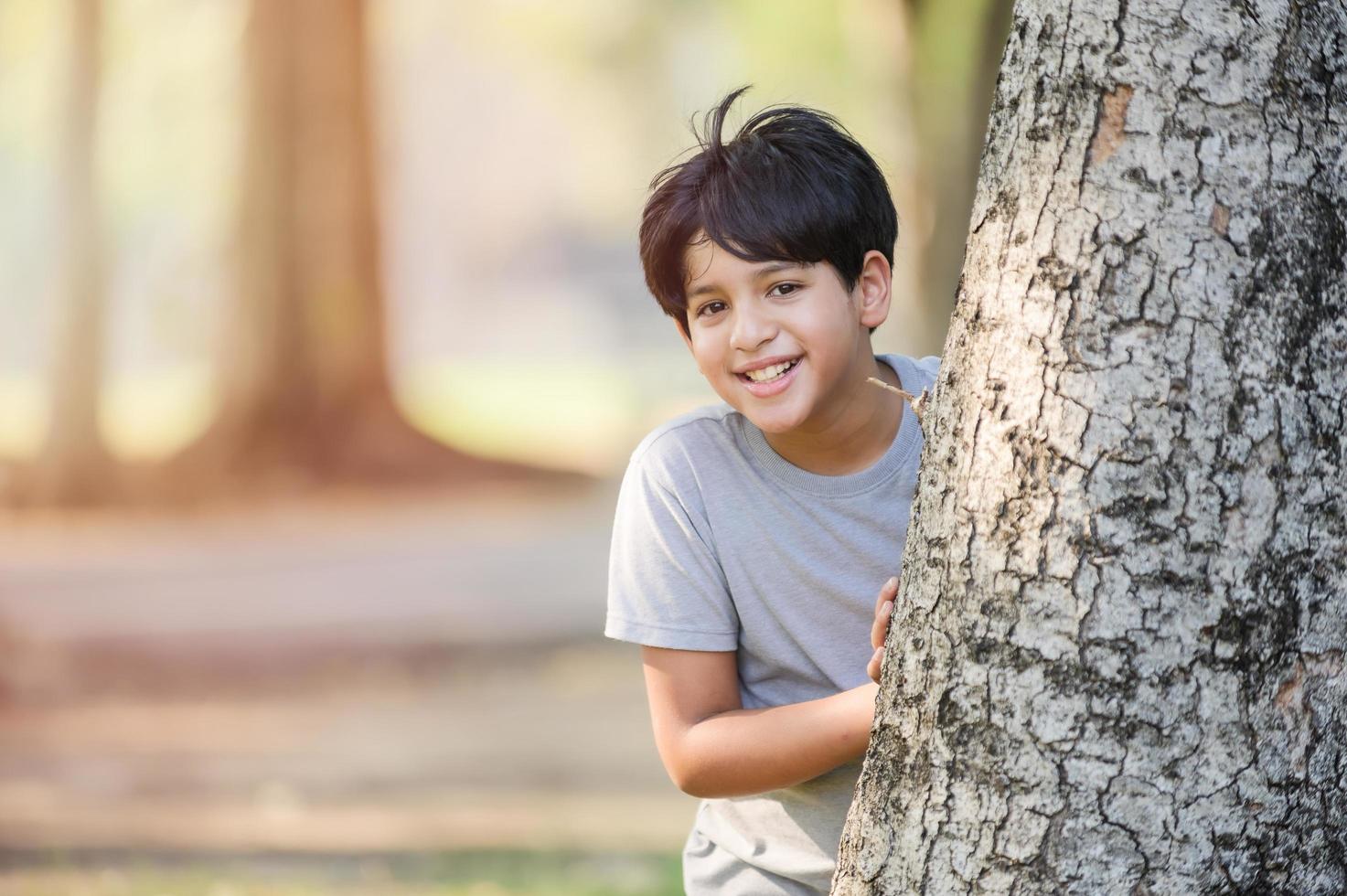 ein halbthailändischer Junge spielt heimlich hinter einem großen Baum in einem Park, während er außerhalb der Schule lernt foto