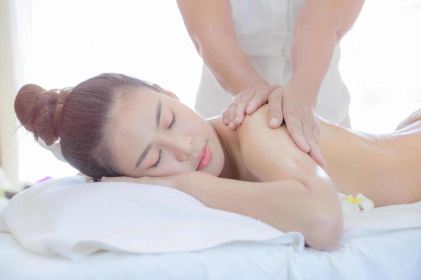 eine schöne asiatische frau entspannt sich bequem in einem spa-shop, nachdem die masseurin ihren körper massiert hat foto