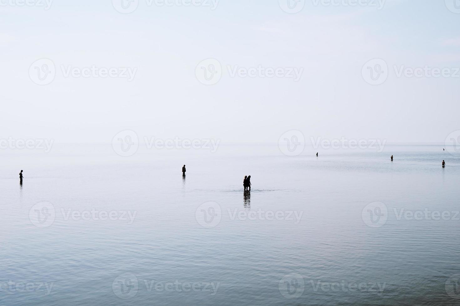 Silhouetten von Menschen, die durch seichtes Wasser gehen und waten foto