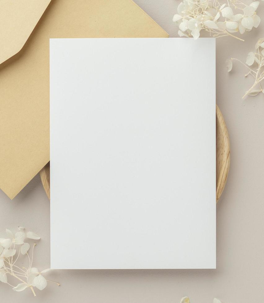 leere Grußkarten-Einladungsmodell 5x7 auf Umschlag mit trockenen Blumen und Band auf Papierhintergrund, flache Lage, Modell foto