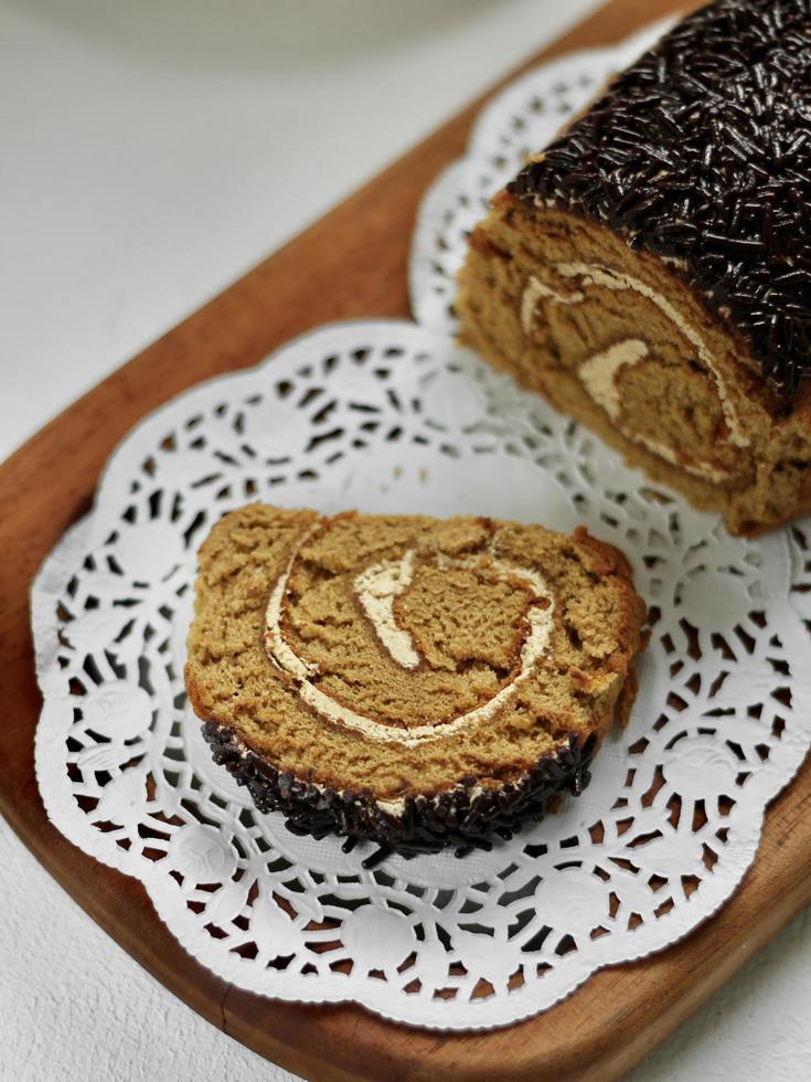 Nahaufnahme von Mokka-Schokorollenkuchen auf rustikalem Papier und Holzschneidebrett. foto