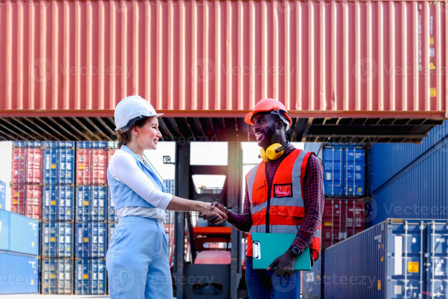 zwei arbeiter mit schutzhelm schütteln sich die hände auf dem hof der logistischen schiffsfrachtcontainer. afroamerikanischer ingenieurmann, der nach der arbeitsdiskussion mit seiner schönen jungen chefin eine handhütte hat foto