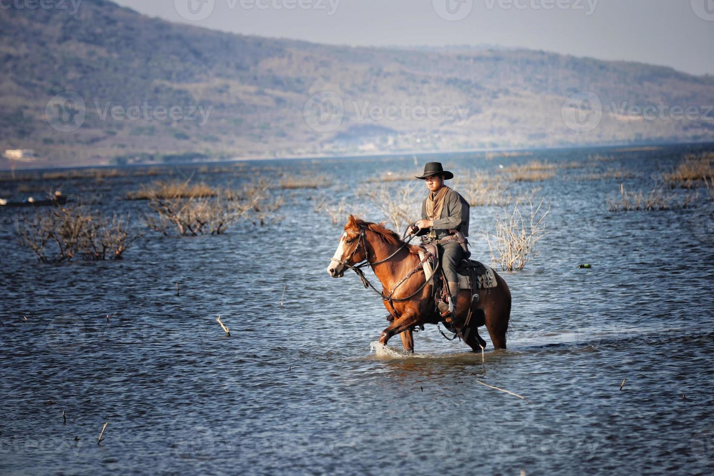 Cowboy zu Pferd vor einem wunderschönen Sonnenuntergang, Cowboy und Pferd im ersten Licht, Berg, Fluss und Lifestyle mit natürlichem Lichthintergrund foto