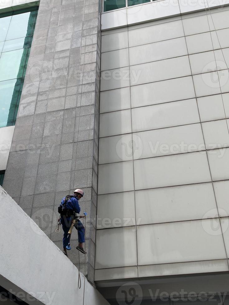 Foto eines Arbeiters, der die Außenseite des Gebäudes reinigt und an einem Sicherheitsseil hängt