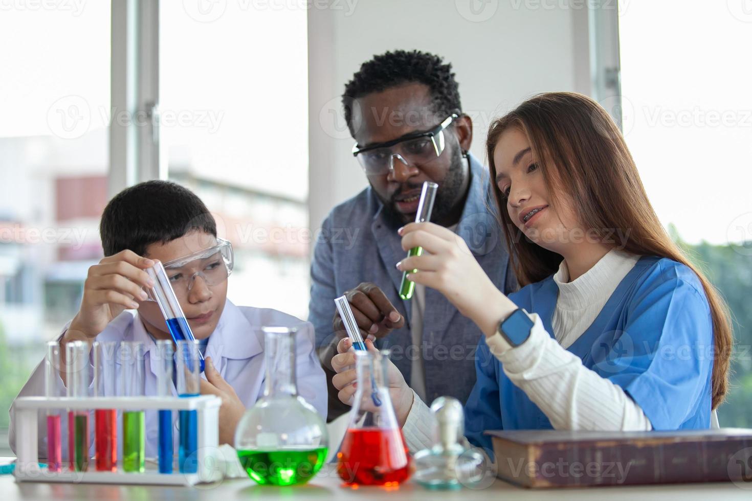 Studenten mischen Chemikalien in Bechergläsern. begeisterter lehrer erklärt kindern chemie, chemiestudent zeigt dem naturwissenschaftsunterricht ein neues experiment foto