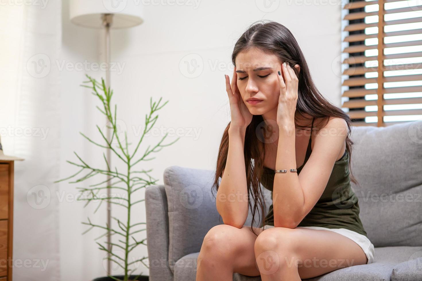 traurige depressive junge frau zu hause, die auf dem sofa sitzt. frustriertes und unglückliches Mädchen mit schrecklicher Migräne oder Kopfschmerzen. foto