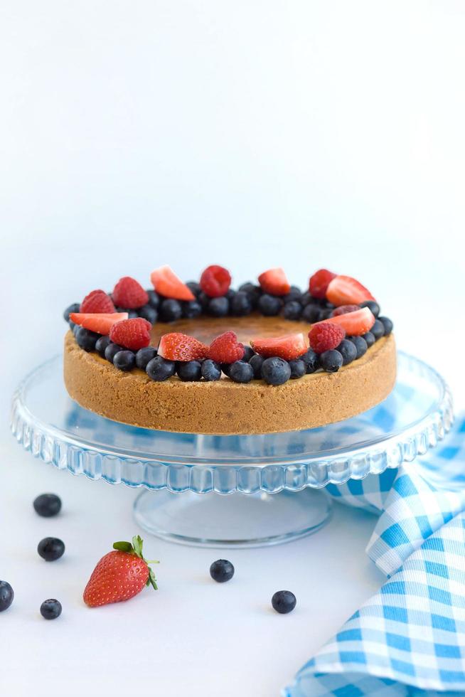 Käsekuchen mit Beeren auf einem Glasständer auf hellem Hintergrund mit blauer Serviette foto