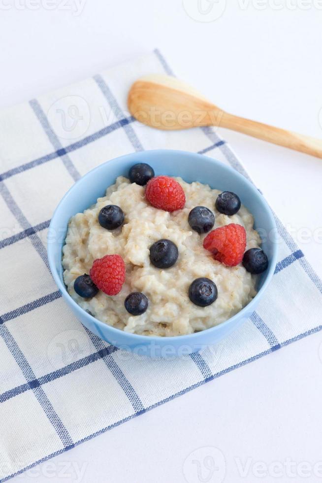 Haferbrei mit Beeren zum Frühstück. Haferflocken in einem blauen Teller mit einem Holzlöffel auf dem Tisch von oben foto