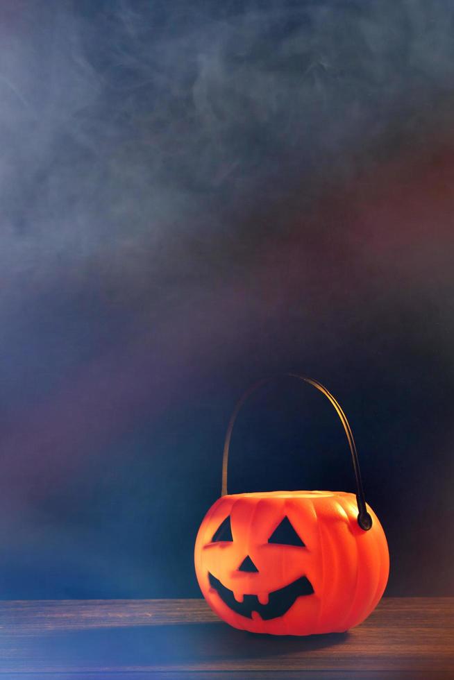 halloween-konzept - orangefarbene plastikkürbislaterne auf einem dunklen holztisch mit verschwommenem funkelndem licht im hintergrund, süßes oder saures, nahaufnahme. foto
