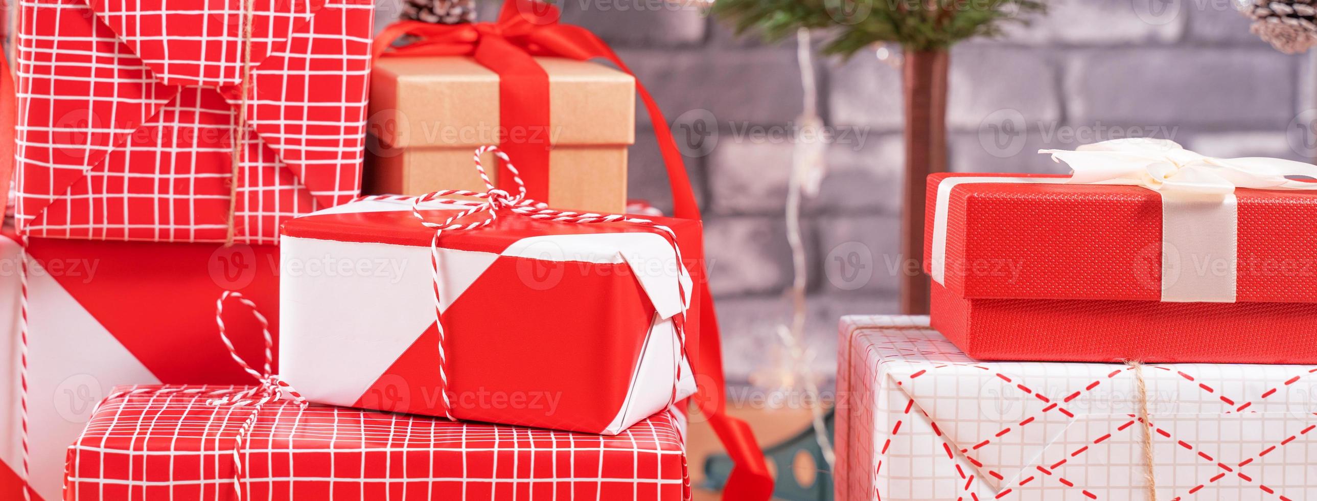 geschmückter weihnachtsbaum mit eingewickelten schönen roten und weißen geschenken zu hause mit schwarzer backsteinmauer, festliches designkonzept, nahaufnahme. foto