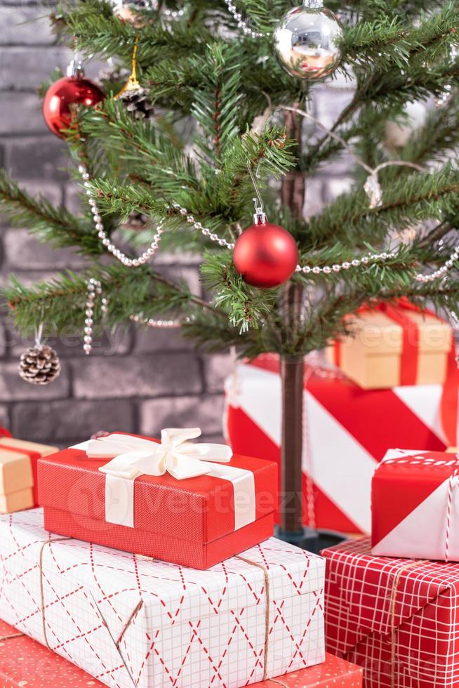 geschmückter weihnachtsbaum mit eingewickelten schönen roten und weißen geschenken zu hause mit schwarzer backsteinmauer, festliches designkonzept, nahaufnahme. foto