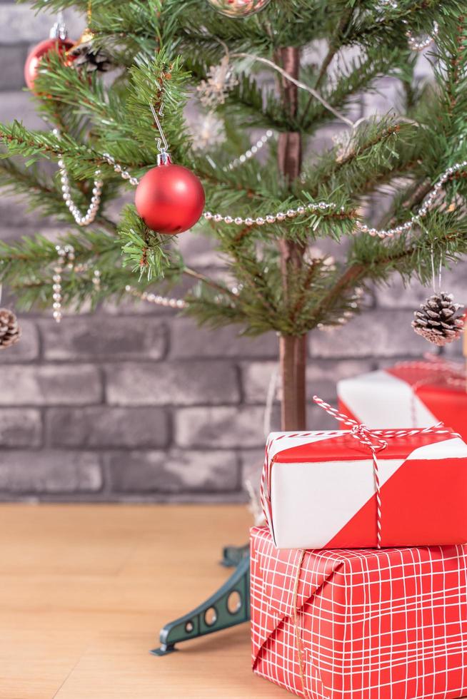 geschmückter weihnachtsbaum mit eingewickelten schönen roten und weißen geschenken zu hause mit schwarzer backsteinmauer, festliches designkonzept, nahaufnahme. foto