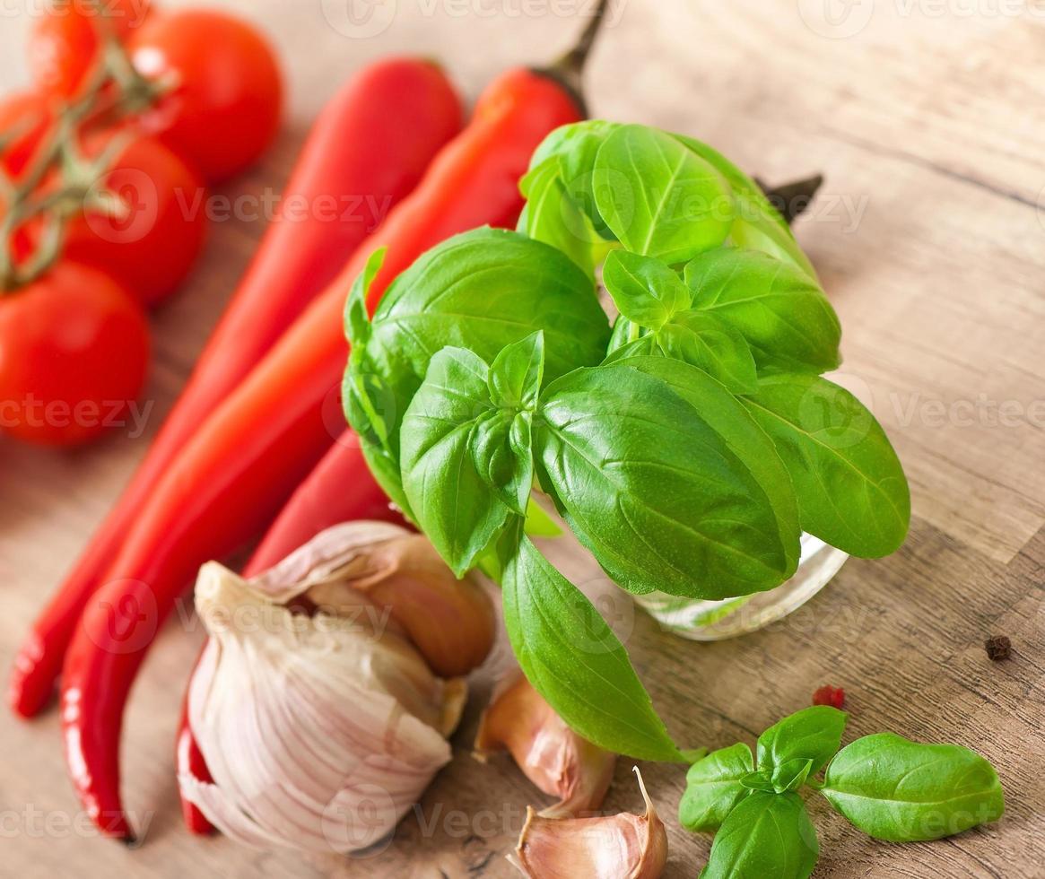 rote Chilischoten, Tomaten, Knoblauch und Basilikum auf Holzhintergrund foto