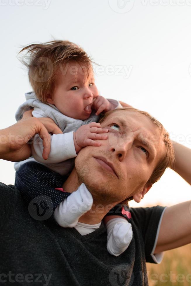 eine kleine süße tochter sitzt auf ihrem hals in der nähe ihres vaters. Vater und Tochter gehen auf dem Feld spazieren foto