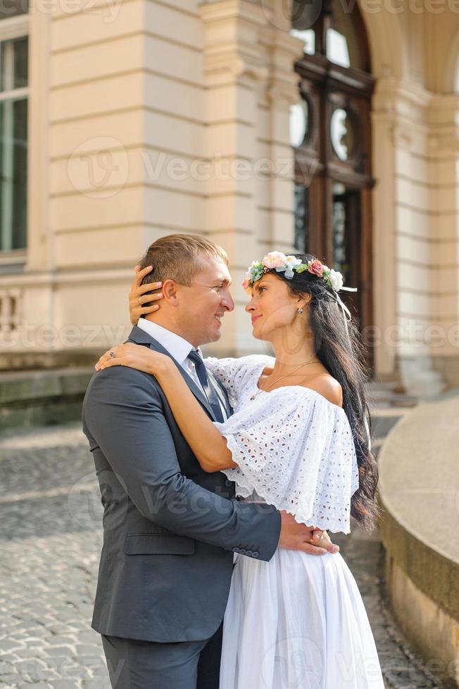 Hochzeitsfotosession auf dem Hintergrund des alten Gebäudes. der bräutigam sieht seiner braut beim posieren zu. rustikale oder Boho-Hochzeitsfotografie. foto