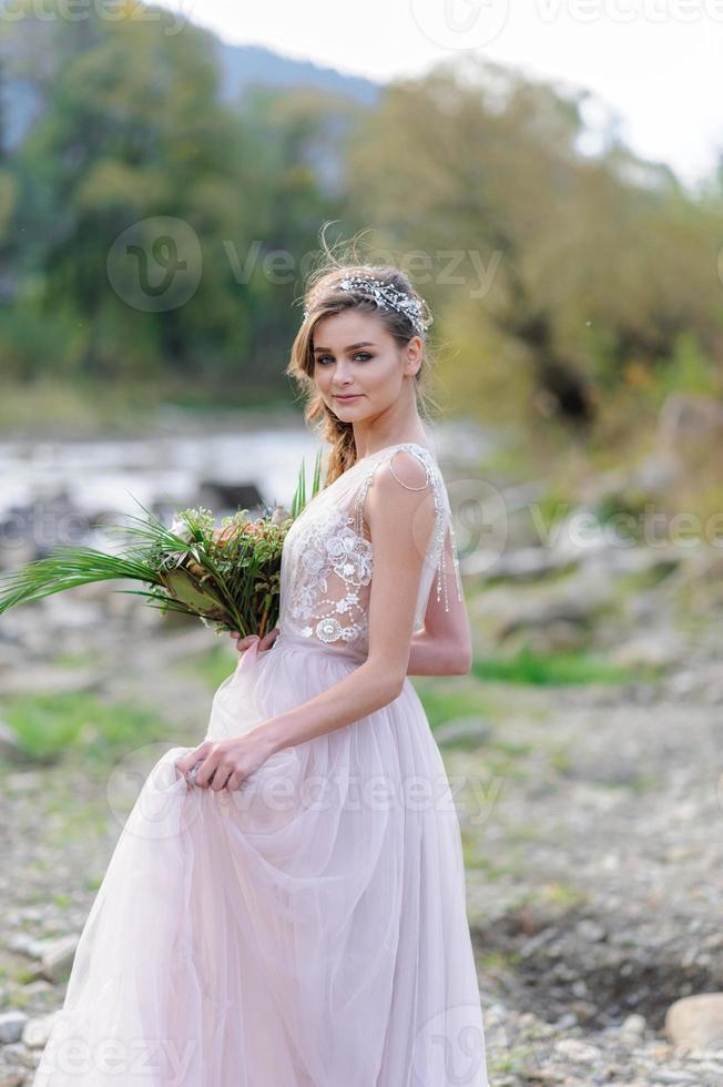 glückliche Braut in einem rosa Hochzeitskleid. das mädchen hält einen hochzeitsstrauß in ihren händen. Hochzeitszeremonie im Boho-Stil im Wald. foto