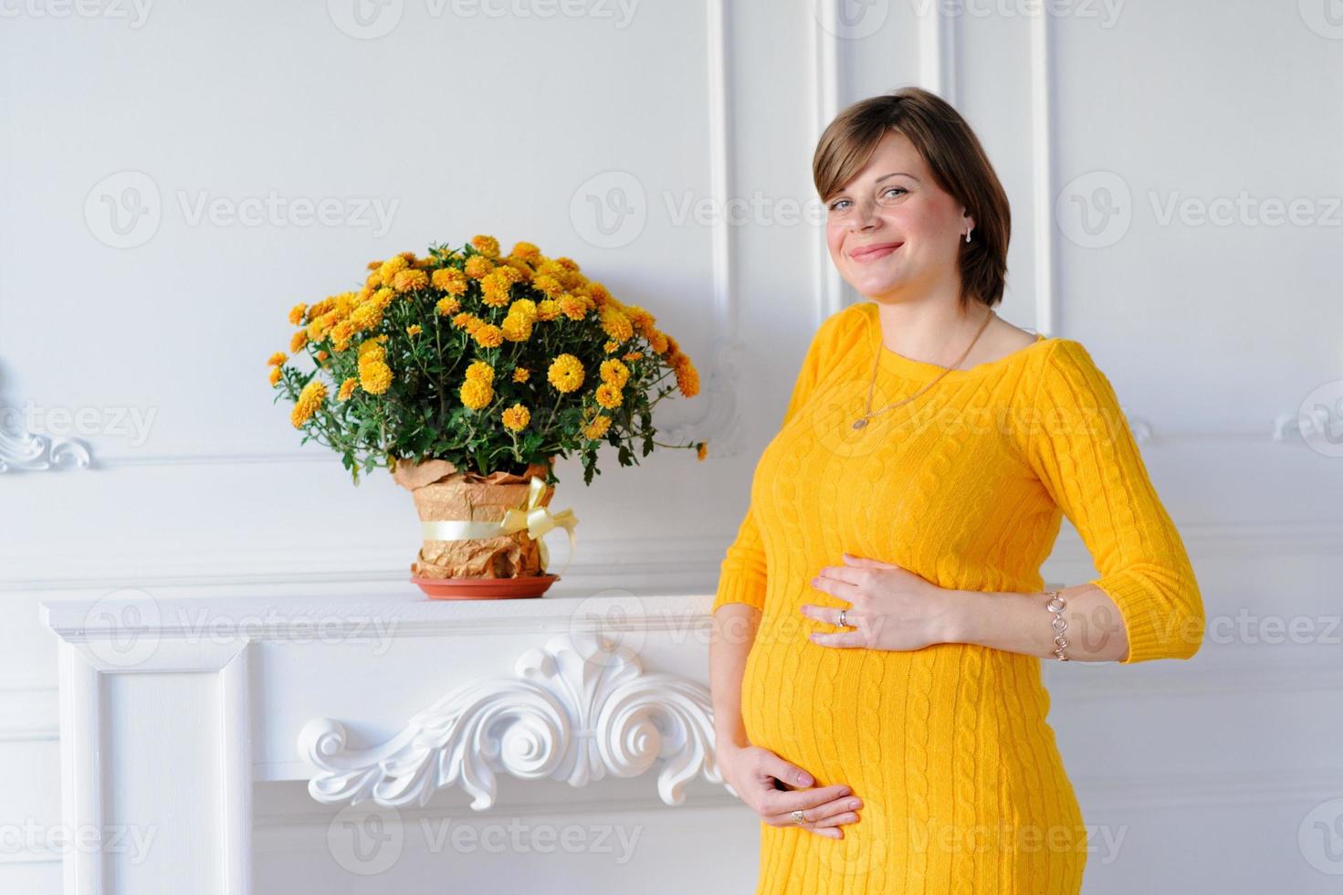 Glückliche schwangere Frau in einem gelben Kleid hält ihren Bauch. foto