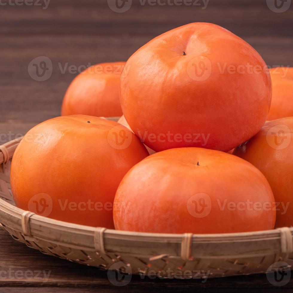 frische, schöne orangefarbene Kaki-Kaki auf Bambussieb über dunklem Holztisch. saisonale, traditionelle frucht des chinesischen mondneujahrs, nahaufnahme. foto